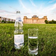 Mineralwasserflasche und Glas auf Wiese vor Reichstagsgebäude